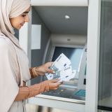 glad-pretty-millennial-islamic-female-in-hijab-counting-many-euros-near-atm-outdoor-e1706686204385.jpg